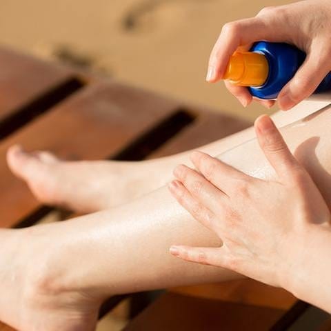 Eine Frau reibt sich die Beine mit Sonnencreme ein