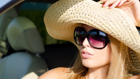 Frau mit Strohhut und Sonnenbrille schützt sich vor UV-Strahlen