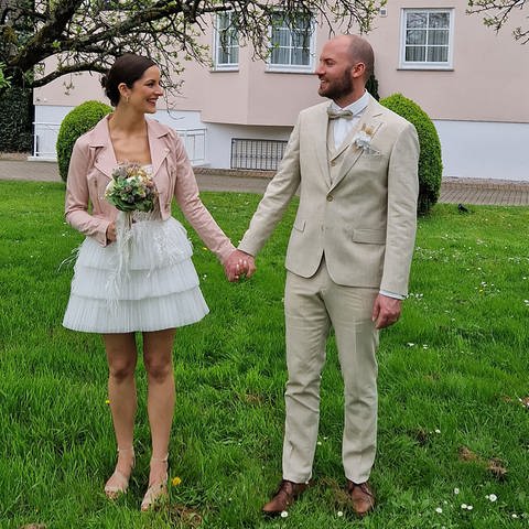 Paar im Garten zeigt Brautkleid und Anzug für die Hochzeit (Foto: Brautsalon Lecher)