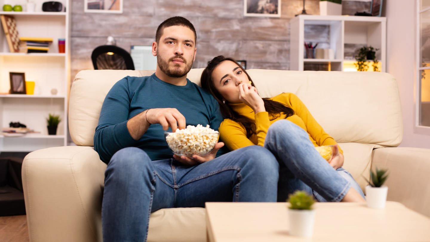Paar sitzt vor dem Fernseher und isst Popcorn