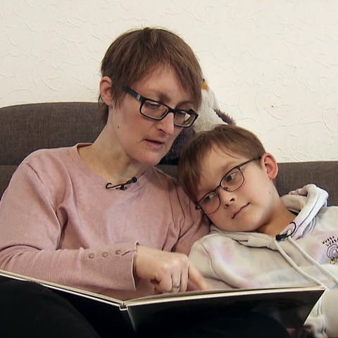 Mama sitzt mit Kind auf dem Sofa und schauen  hören ein Buch an (Foto: SWR)