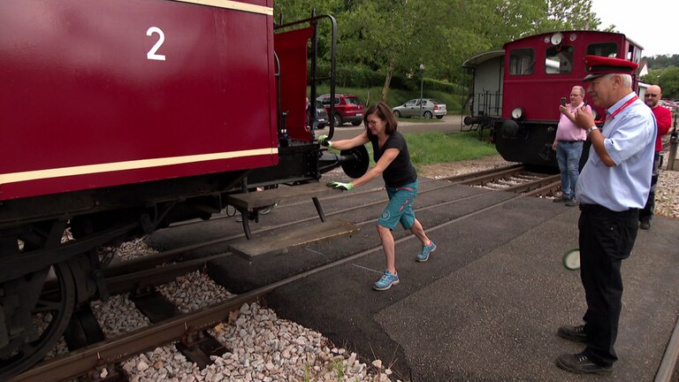 Eine Frau schiebt einen Eisenbahnwagon und ein Schaffner pfeifft  (Foto: SWR)