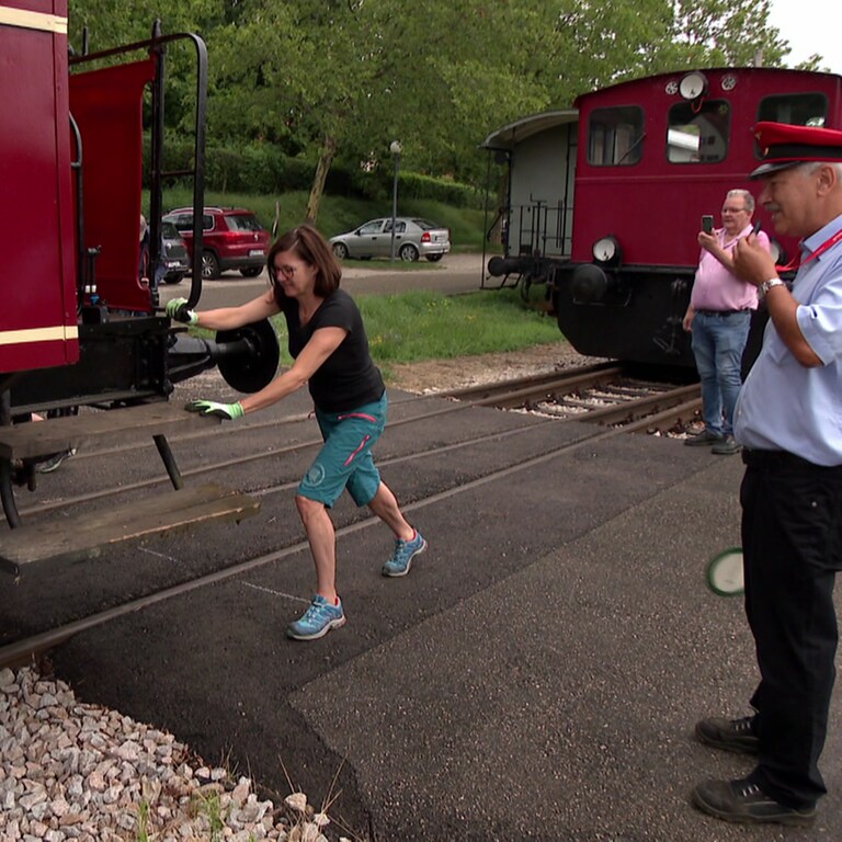Eine Frau schiebt einen Eisenbahnwagon und ein Schaffner pfeifft  (Foto: SWR)