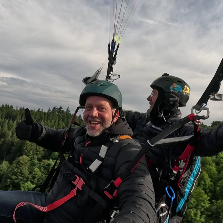Zwei Männer sind an einem Fallschirm in der Luft und zeigen Daumen nach oben (Foto: SWR)