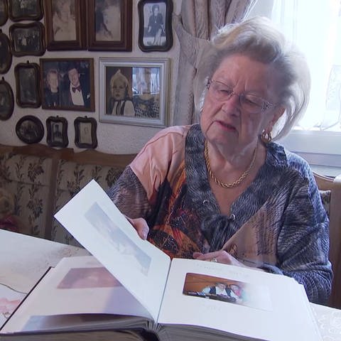 Ältere Frau zeigt ein Fotoalbum an einem Tisch