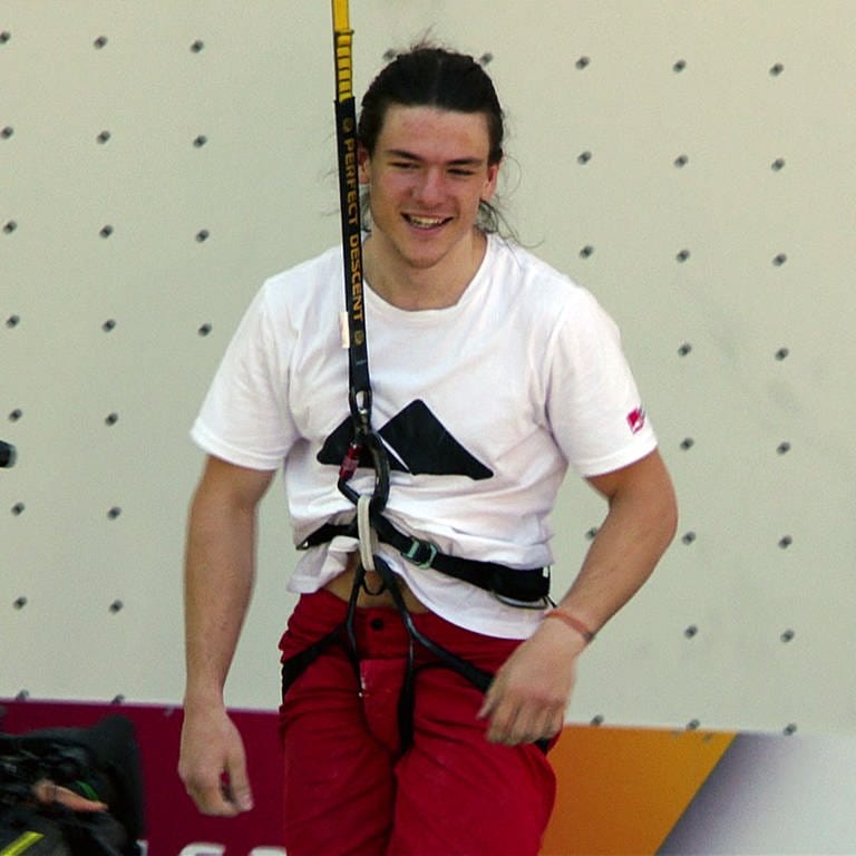 Adrian steht mit einem Seil gesichert vor einer Kletterwand und lacht 