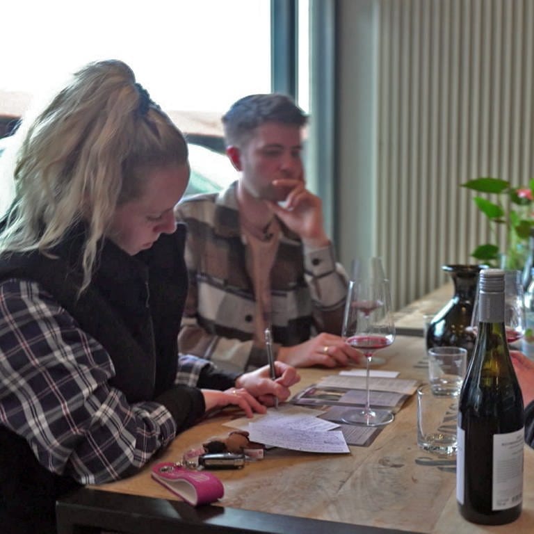 Annika und Manuel Braun sitzen bei einer Weinprobe mit einem Winzer am Tisch