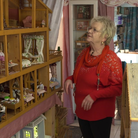 Eine alte Dame steht im Keller vor den Puppenhäusern, die sie gebaut hat.