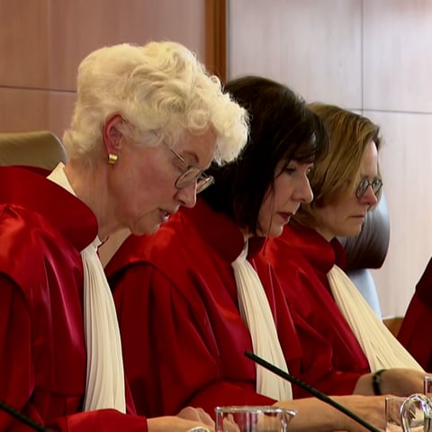 5 Richter im Richtersaal in roten Roben.