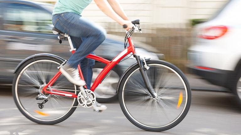 Eine Person fährt auf einem roten Fahrrad an ein paar Autos vorbei