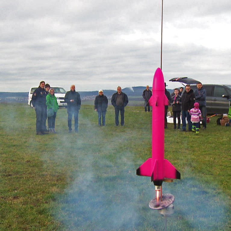 Ein pinkes Raketenmodell wird auf einer Wiese gezündet
