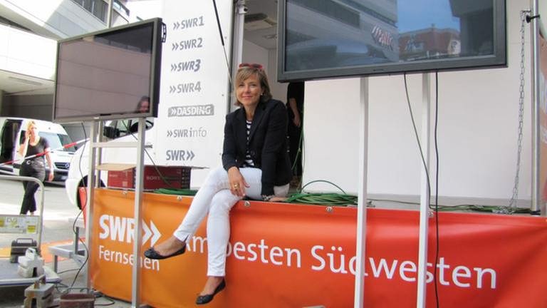 Moderatorin Annette Krause sitzt auf einer mobilen Bühne vor einem SWR-Transporter