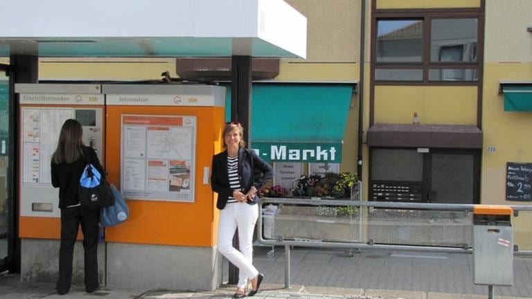 Moderatorin Annette Krause lehnt an Fahrkartenautomat an Bahnhaltestelle