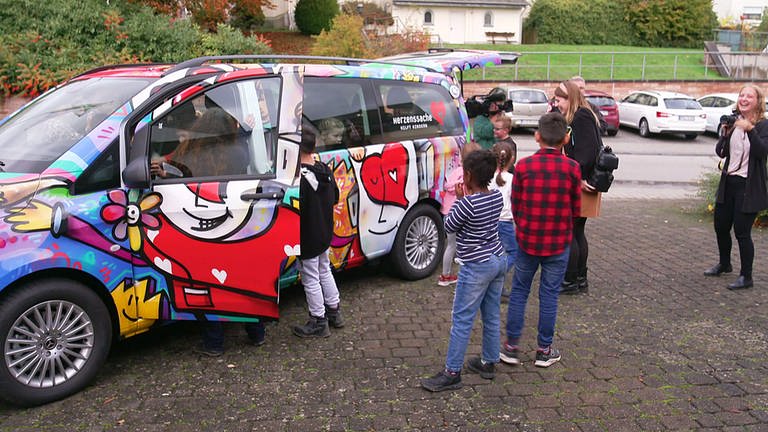 Überraschung gelungen: Die Mitarbeiter*innen und Kinder vom Café International in Büchenbeuren freuen sich über ihren neuen Bus. (Foto: SWR)