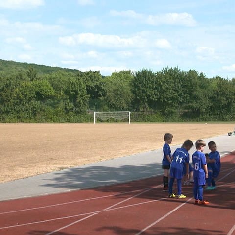 Links der vertrocknete Hybridrasenplatz. Die Kinder im Fußballverein spielen auf der Rennbahn.