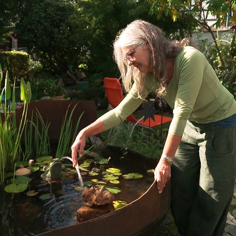 Eine ältere Frau steht im Garten an ihrem Brunnenteich (Foto: SWR)