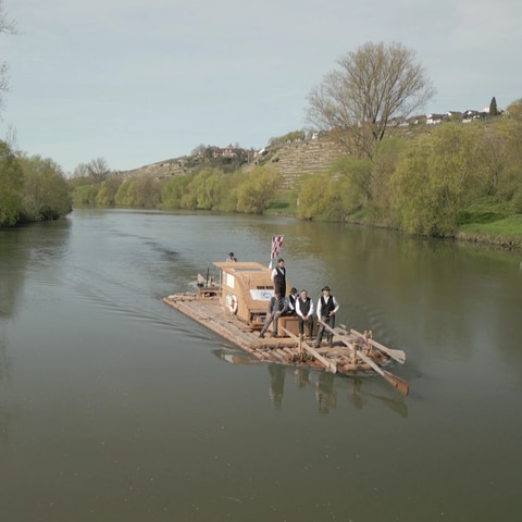 Auf einem hölzernen Floß fahren mehrere Männer den Neckar entlang.