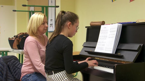 Musiklehrerin sitzt am Klavier neben spielender Schülerin (Foto: SWR)