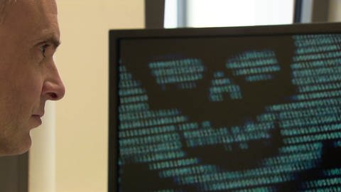 Mann im Profil sichtbar schaut auf Computer-Monitor mit einer Totenkopf-Darstellung (Foto: SWR)