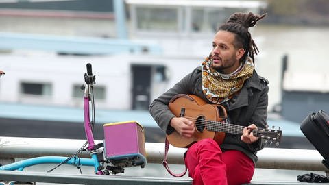 Weltbürger Imran Khan in Mainz zu Hause. Er sitzt am Rhein in Mainz und spielt auf seiner Gitarre. (Foto: SWR, SWR)