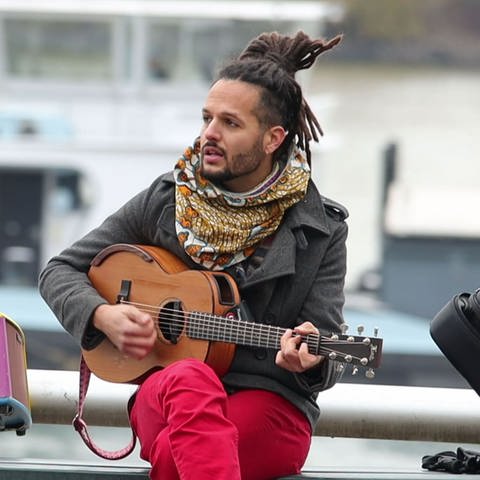 Weltbürger Imran Khan in Mainz zu Hause. Er sitzt am Rhein in Mainz und spielt auf seiner Gitarre. (Foto: SWR, SWR)