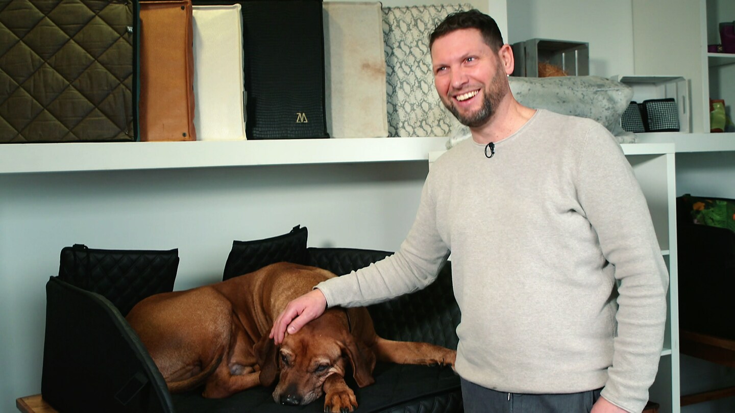 Björn Wiltholt neben einem braunen Hund auf einem Hundebett. (Foto: SWR)
