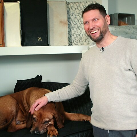 Björn Wiltholt neben einem braunen Hund auf einem Hundebett. (Foto: SWR)