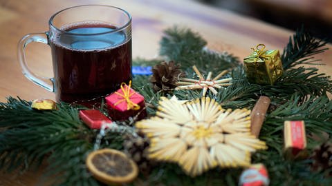 Ein Glas roter Glühwein steht neben einem Weihnachtsgesteck. (Foto: dpa Bildfunk, picture alliance / Arno Burgi/dpa-Zentralbild/dpa)