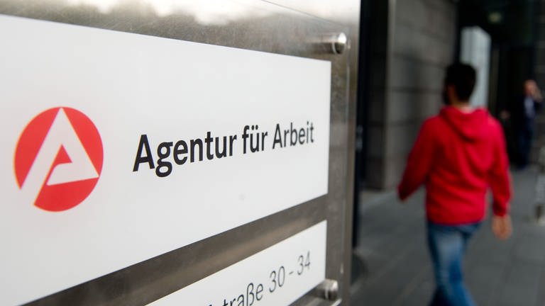 Ein Mann geht hinter dem Schild der Agentur für Arbeit in Stuttgart zum Eingang. (Foto: dpa Bildfunk, picture alliance / Sebastian Kahnert/dpa)