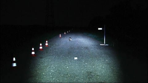 Ein Feldweg, der von einer Fahrradlampe ausgeleuchtet wird. (Foto: SWR)