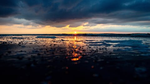 Die Sonne geht am Strandabschnitt "Weiße Düne" über der Nordsee unter und spiegelt sich dabei in den Wellen. (Foto: dpa Bildfunk, picture alliance/dpa | Hauke-Christian Dittrich)