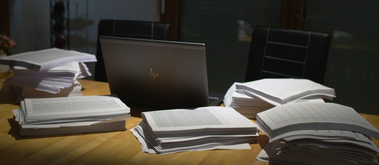 Mehrere Stapel Papier liegen um einen Laptop herum auf einem Tisch. (Foto: SWR)