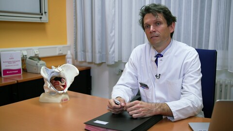 Prof. Markus Hübner, Urogynäkologe am Uniklinikum Freiburg, sitzt an einem Tisch, neben ihm das Model eines Beckenbodens (Foto: SWR)