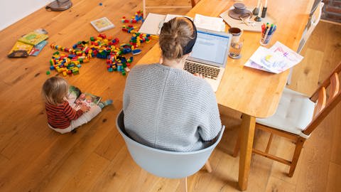 Frau sitzt arbeitend an PC neben spielendem Kind. Doppelbelastung im Homeoffice. (Foto: dpa Bildfunk, picture alliance/dpa | Julian Stratenschulte)