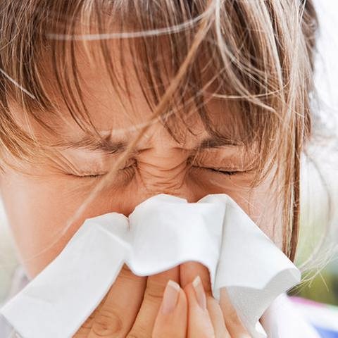 Frau niest aufgrund von Heuschnupfen in ein Taschentuch. (Foto: Getty Images, Thinkstock - Meggj)