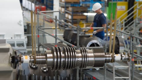 Ein Arbeiter steht in einer Montagehalle des Siemens-Turbinenwerks. Im Vordergrund hängt eine Turbine in der Montage. (Foto: dpa Bildfunk, picture alliance/Sebastian Kahnert/zb/dpa)