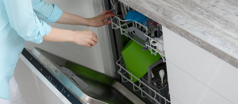 Eine Frau öffnet eine Spülmaschine. In der Spülmaschine ist Geschirr, auf der Arbeitsplatte stehen Küchenutensilien herum. (Foto: Colourbox)