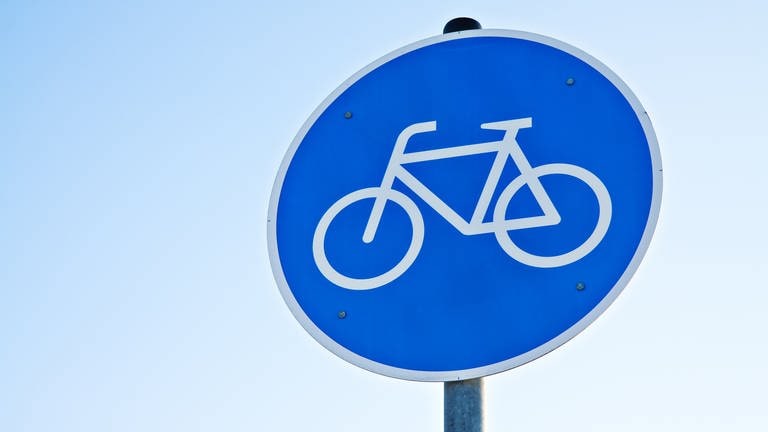 Auf einem blauen Schild ist ein weißes Fahrrad abgebildet. Es handelt sich um das Verkehrszeichen, das einen Fahrradweg anzeigt. (Foto: Colourbox)