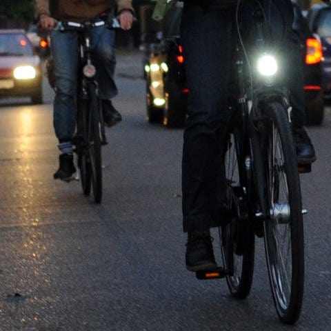 Ein Fahrradfahrer mit Licht und einer ohne sind in der Dämmerung auf einer Straße unterwegs: Welche Vorschriften müssen Fahrradleuchten erfüllen? (Foto: dpa Bildfunk, Picture Alliance)