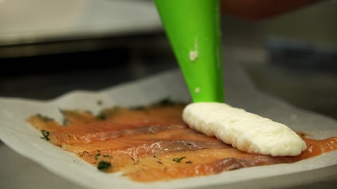 Auf dünn geschnittenden Lachs wird ein Parmesanmousse gespritzt