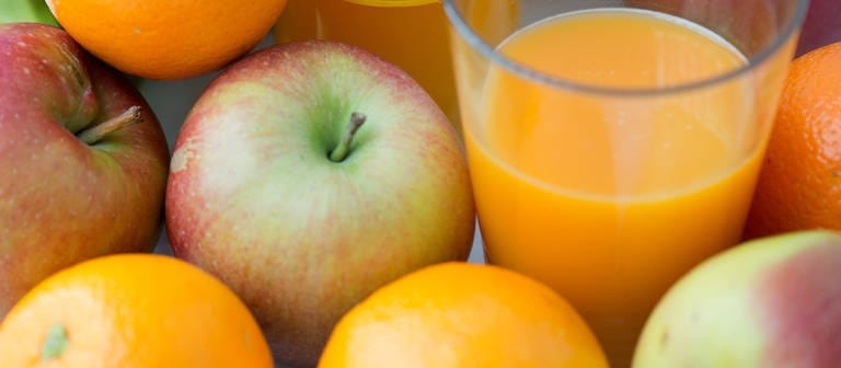 Ein Glas mit Fruchtsaft aus einer Flasche steht inmitten von Äpfeln und Orangen. (Foto: dpa Bildfunk, picture alliance / dpa | Arno Burgi)