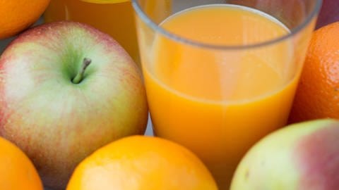 Ein Glas mit Fruchtsaft aus einer Flasche steht inmitten von Äpfeln und Orangen. (Foto: dpa Bildfunk, picture alliance / dpa | Arno Burgi)