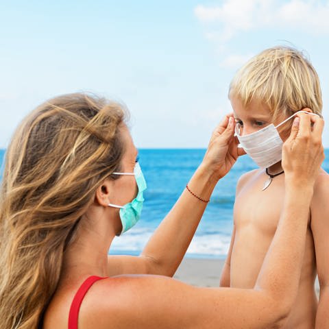 Mutter setzt Sohn am Strand Gesichtsmaske auf. (Foto: Colourbox)