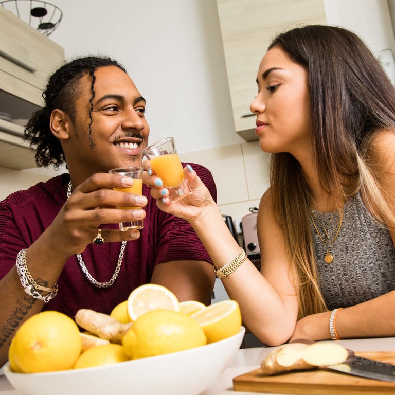 Ein Paar hält am Küchentisch Ingwer-Shots mit Zitrone und Apfel in den Haenden und prostet sich zu. (Foto: dpa Bildfunk, picture alliance / dpa-tmn | Christin Klose)