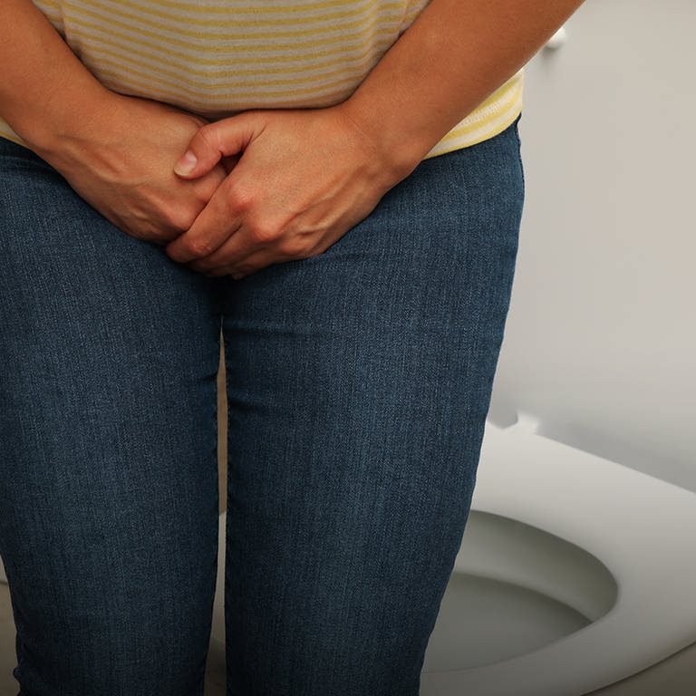Eine Frau steht vor einer Toilette und hält sich den Unterleib. Blasenentzündung kann schmerzhaft sein.