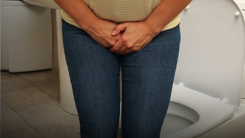 Eine Frau steht vor einer Toilette und hält sich den Unterleib. Blasenentzündung kann schmerzhaft sein. (Foto: Colourbox, Colourbox49202517)