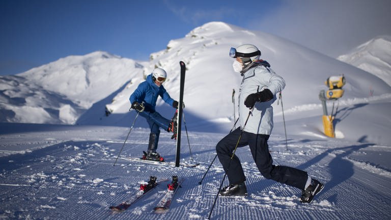 Skifahrer, einer mit Maske, wärmen sich mit Kniebeugen und Gymnastik auf (Foto: dpa Bildfunk, Picture Alliance)