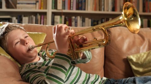Ein Junge liegt auf dem Sofa und spielt Trompete.