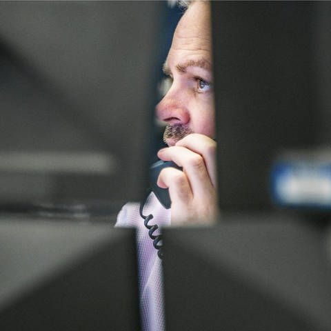 Ein Börsenhändler schaut mit dem Telefonhörer am Ohr auf Computermonitore (Foto: dpa Bildfunk, dpa/Frank Rumpenhorst 246843476)
