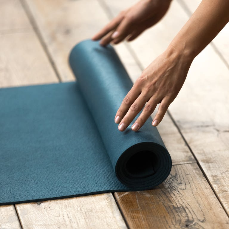 Eine Frau rollt eine Yogamatte auf dem Boden aus. Was sollte man beim Fitnessmatten-Kauf beachten? (Foto: Colourbox, COLOURBOX35709981)